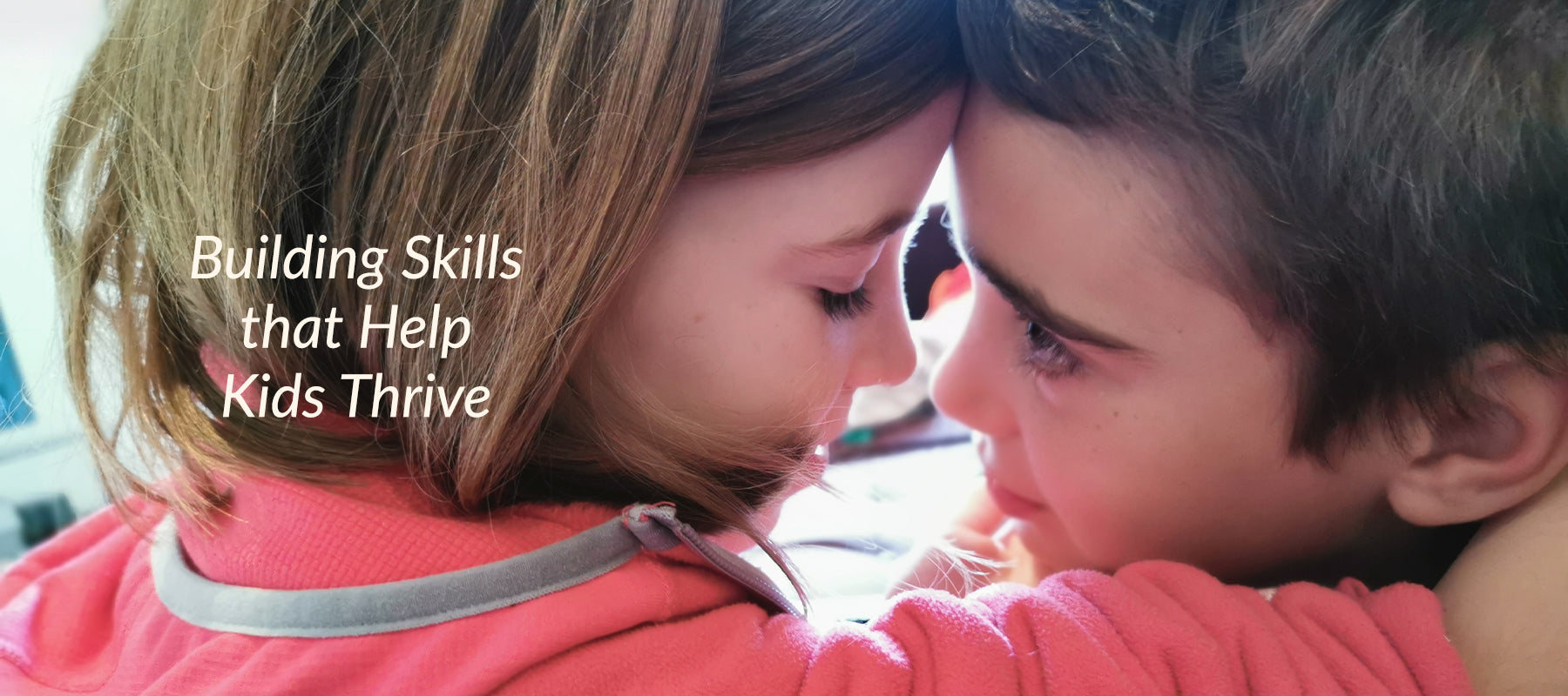 A young girl dressed in a bright pink jersey hugs her brother with their foreheads touching. The words 'Building Skills that Help Kids Thrive' sits in the foreground. 